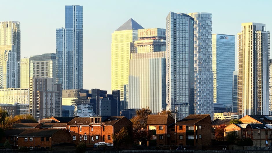 A view of a modern city skyline featuring numerous tall glass and steel skyscrapers and office buildings, with some displaying company logos such as HSBC and Citi. In the foreground, there is a row of