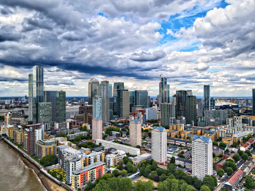 A view of a modern city skyline featuring numerous tall glass and steel skyscrapers and office buildings, with some displaying company logos such as HSBC and Citi. In the foreground, there is a row of